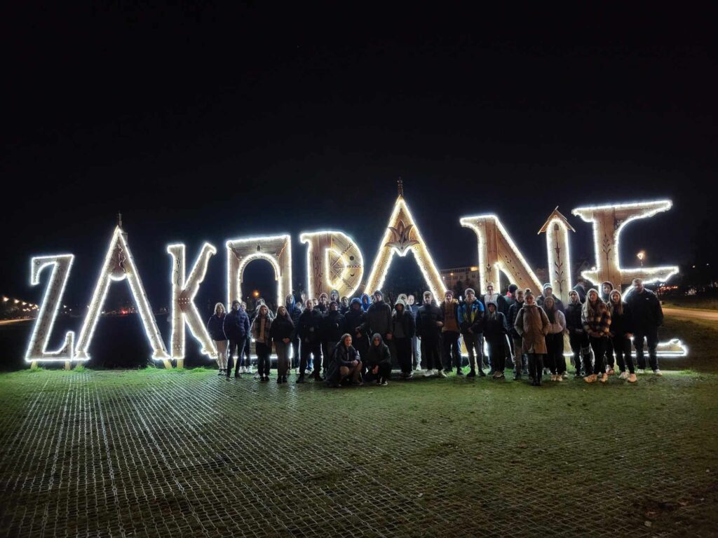 Uczestnicy wycieczki na tle świetlnego napisu ZAKOPANE