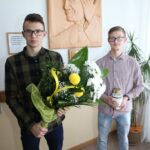 Uczniowie z kwiatami pod płaskorzeźbą Jana Pawła II