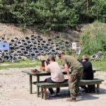 Uczniowie podczas strzelania zza stołu z pomocą instruktora